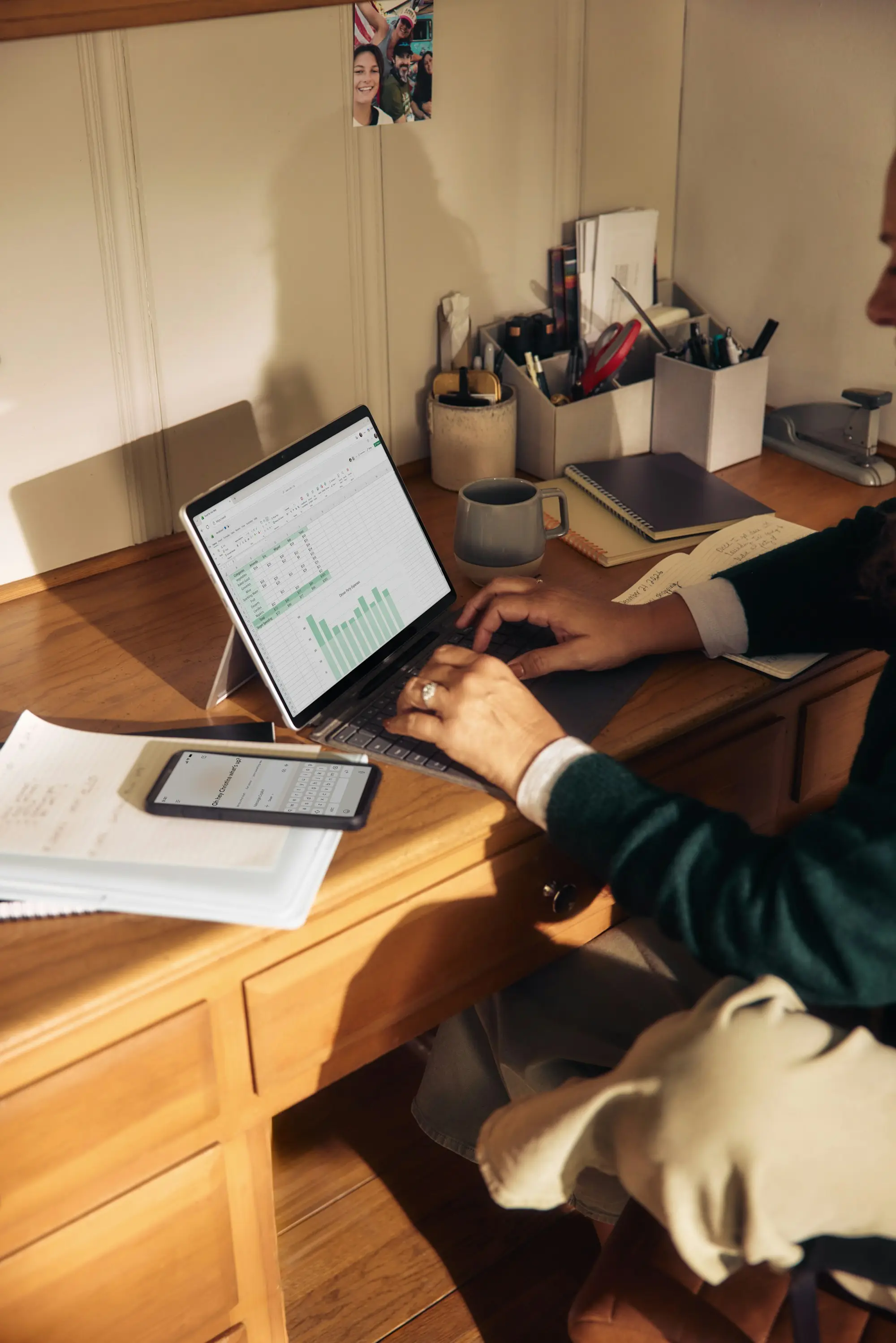 A marketer working alone at a wooden desk with a laptop, notebook and tablet